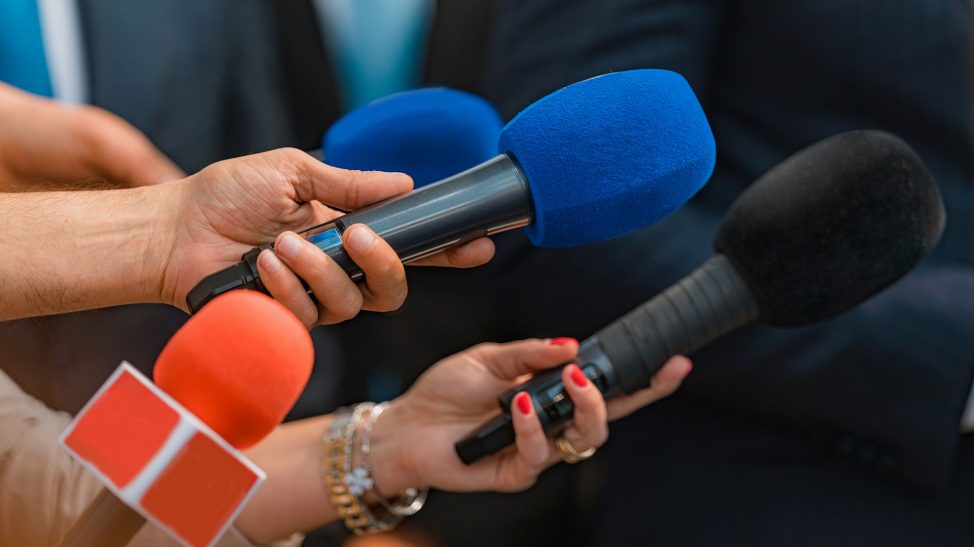 Journalists' hands holding microphones during an interview.